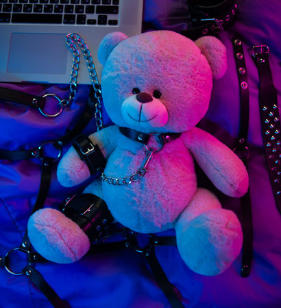 toy bear dressed in leather belts harness accessory for BDSM games on a dark background in neon...