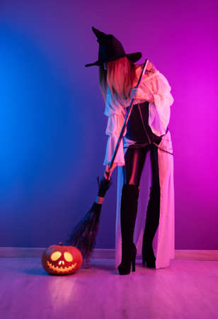 a girl in a witch costume for Halloween with a broom and a pumpkin in neon lightの写真素材