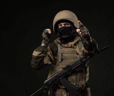 a Russian soldier in military clothes with a assault rifle on a dark background takes orders on a...