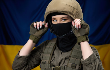 a girl Ukrainian soldier on the background of the flag of Ukraine, wearing a helmet and a bulletproof vestの写真素材