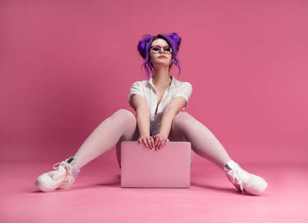 sexy girl with glasses and purple hair with a laptop on a pink backgroundの写真素材