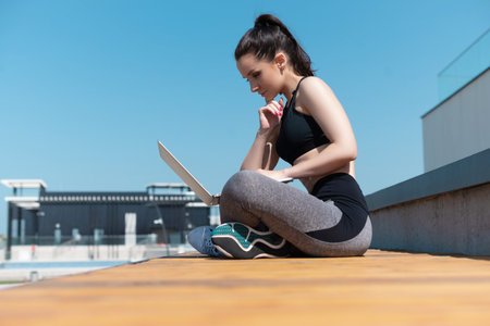 girl in sportswear on a summer outdoor sports field is sitting with a laptop
