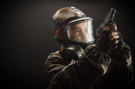 a little boy a child in a gas mask with a gun on a black background
