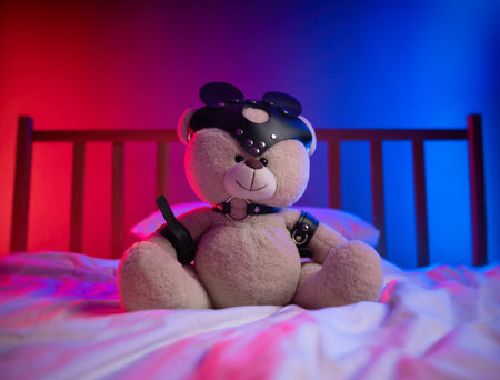 bdsm straps for sex games on a teddy bear in neon light on the bed