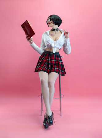 a seductive girl with glasses in a sexy schoolgirl costume and stockings on a pink backgroundの写真素材