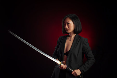 portrait of an Asian girl with a katana in her hands posing emotionally on a black background copy pasteの写真素材