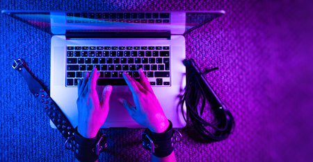 female sexy hands in bdsm handcuffs with laptop in neon light on dark backgroundの写真素材