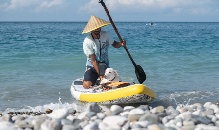 a guy on a sup board with a paddle with a dog stands on the sea in summer