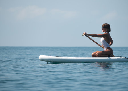 Sexy girl in swimsuit on sup board under the bright sun on the background of the sea , Stand up paddleboardingの写真素材