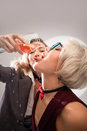 two close girlfriends with glasses of alcohol having fun laughing at a party in the studio on a white background copy pasteの写真素材