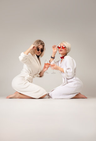two girls in white coats and glasses with glasses of alcohol are sitting in the studio on a white background of a copy pasteの写真素材