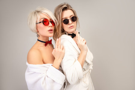 two close friends in white bathrobes and sunglasses stand close to each other and hold their fingers in the shape of a pistolの写真素材