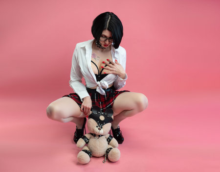 BDSM teddy bear in the hands of a sexy woman in a schoolgirl costume for sexual role-playing games on pink background, copy paste, a banner for a sex shopの写真素材