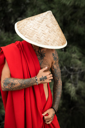 Sexy male monk in red cape and an Asian triangular hat with tattoos in natureの写真素材