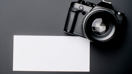 Camera and blank business card on black background. Top view with copy spaceの素材