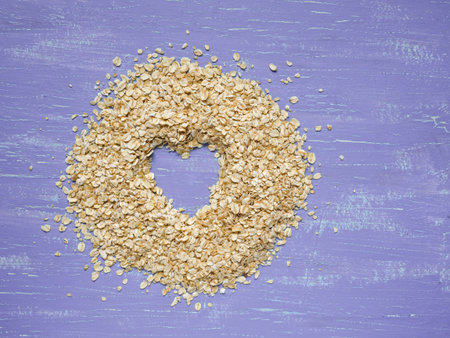 Heap of oat flakes with heart shape on lavender painted background. shot from above