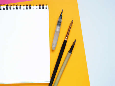 Art table colorful sheet of yellow paper and blank notebook with drawing tools on white background. Top view with copy spaceの写真素材