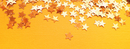 Golden stars glitter on orange paper background. Festive holiday bright backdrop