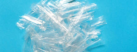 Pile of transparent plastic wrapping rubbish on a blue background. Top view of many plastic wrappings for juice straws with copy space for text. Social media banner or header.の写真素材