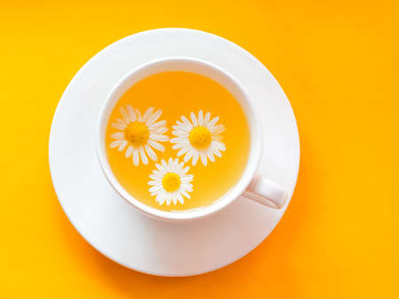 Herbal tea with fresh chamomile flowers in a cup. Cup of medicinal chamomile tea on a bright yellow background. Top viewの写真素材