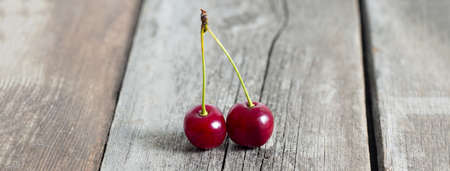 Pair of red ripe cherries on rustic weathered wooden table. Social media banner or header.の写真素材