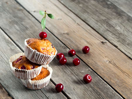 Bunch of freshly baked cherry muffins with fresh berries on a rustic wooden tableの写真素材