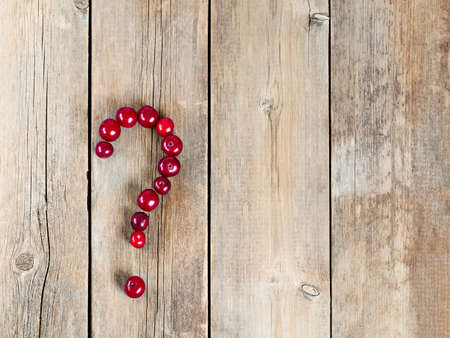 Cherry question symbol on a wooden rustic background. Fresh berries on weathered wooden table. Harvest of Organic fruits.の写真素材