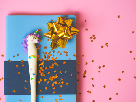 Blue notebook with with cute unicorn pen and gold bow and stars glitter on pink background. Girls...