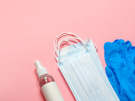 Medical protective mask, latex gloves, hand sanitizer on a pastel pink background. Individual,...