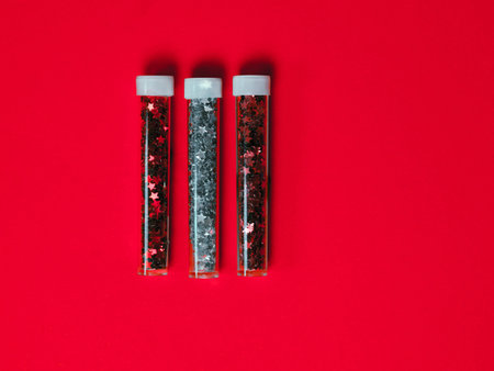 Bottles of festive colored glitter on a red background. Festive twinkle glitter background.