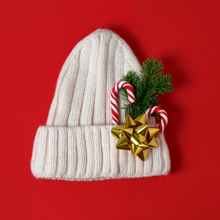 Warm woolen knitted hat decorated with candy cane, evergreen branch and golden bow on a turquoise...