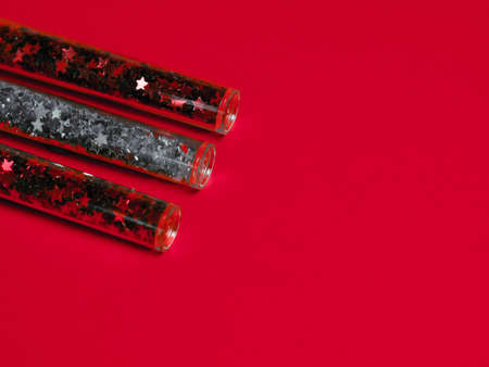 Bottles of festive colored glitter on a red background. Festive twinkle glitter background.の写真素材