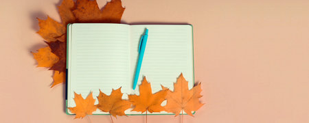 Bright autumn maple leaves with blank notebook on beige paper background. Seasonal fall composition,...