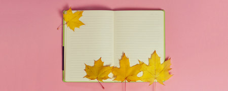Bright autumn maple leaves with blank notebook on pink paper background. Seasonal fall composition,...