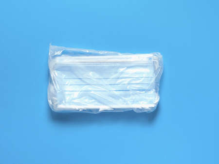 Pack of medical protective masks on a blue paper background. Individual, disposable surgical face mask flat lay pattern. Quarantine healthcare, hygiene and coronavirus protection concept background.の写真素材