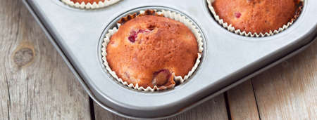 Freshly baked berry muffins closeup in baking tray on a rustic wooden table. Social media banner or header.の写真素材