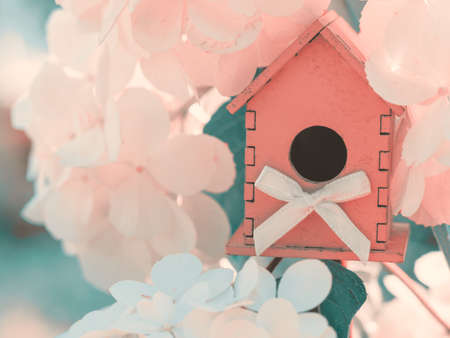 Wooden pink toy house in the white hydrangea flowers against the green background. romantic Valentines day concept.の写真素材