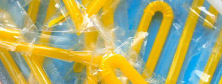 Pile of yellow drinking straws on a blue background. Top view of many plastic bendy cocktail straws, abstract backdrop. Social media banner or header.の写真素材