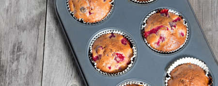 Freshly baked berry muffins closeup in baking tray on a rustic wooden table. Social media banner or header.の写真素材