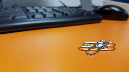 Paperclips on orange desk with blur background keyboard and mouse.の写真素材