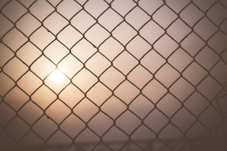 Morning sky at sunrise shining through a metal wire mesh fence.の写真素材