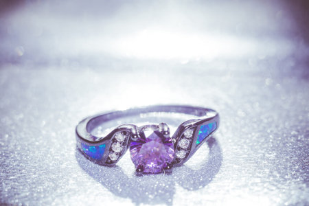 Fashion black gold ring with purple amethyst on glittering background.