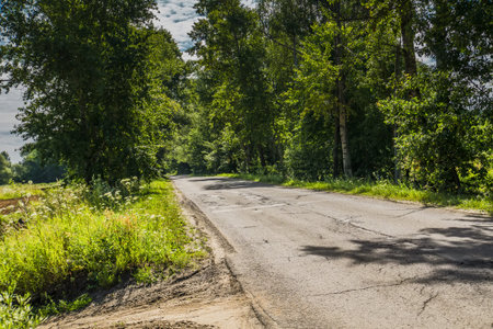 Old cracked, damaged asphalt road in countryside at sunny day.
