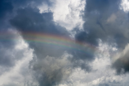 Colorful rainbow against dark cloudy sky background.の写真素材