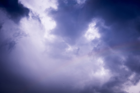Colorful rainbow against dark cloudy sky background.の写真素材