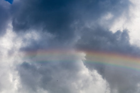 Colorful rainbow against dark cloudy sky background.の写真素材