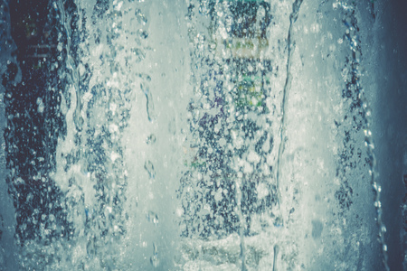 Splashing water in the city park fountain at the summer day, filtered background.の写真素材