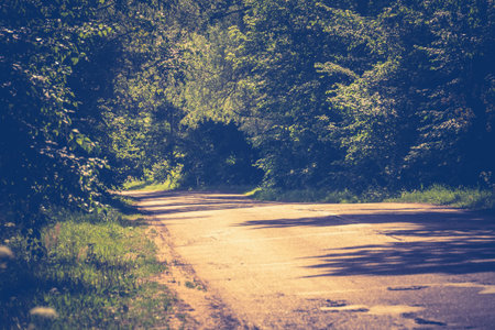 Old cracked, damaged asphalt road in countryside at sunny day, vintage background.