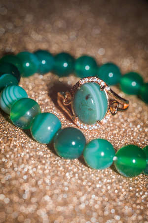 Modern gold ring and beaded bracelet made from green striped agate on glitter background.の写真素材
