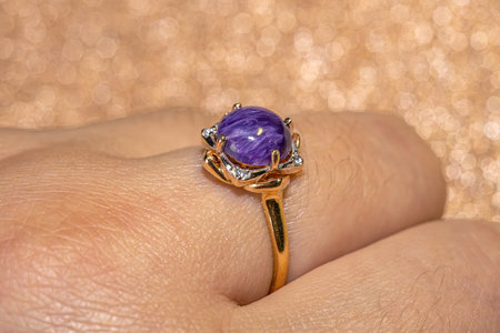 Close up of fashion golden ring decorated with purple stone. Gold ring with natural charoite stone.の写真素材